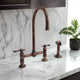 Antique copper kitchen bridge faucet with tall gooseneck spout and separate side sprayer on marble countertop