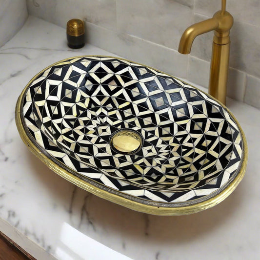 Top view of a handcrafted Moroccan bathroom basin featuring intricate black, white, and gold geometric patterns with brass inlay, set on a marble countertop