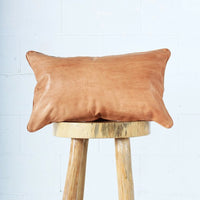 Close-up of a handcrafted leather pillow on a wooden stool, showcasing its texture and quality.
