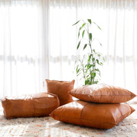 Handcrafted custom leather pillows in tan and light tan, displayed on a rug with natural light.