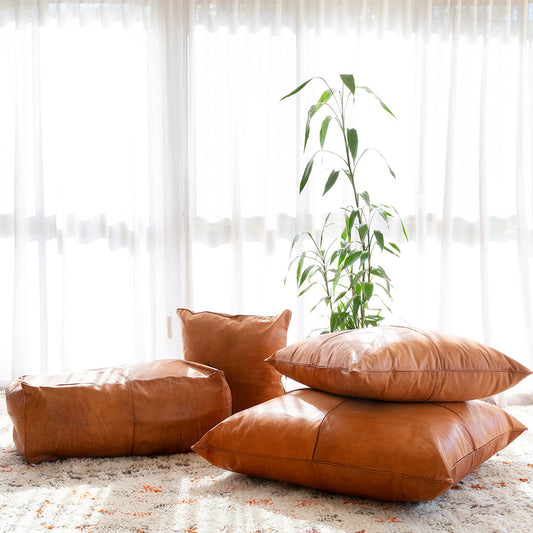 Handcrafted custom leather pillows in tan and light tan, displayed on a rug with natural light.