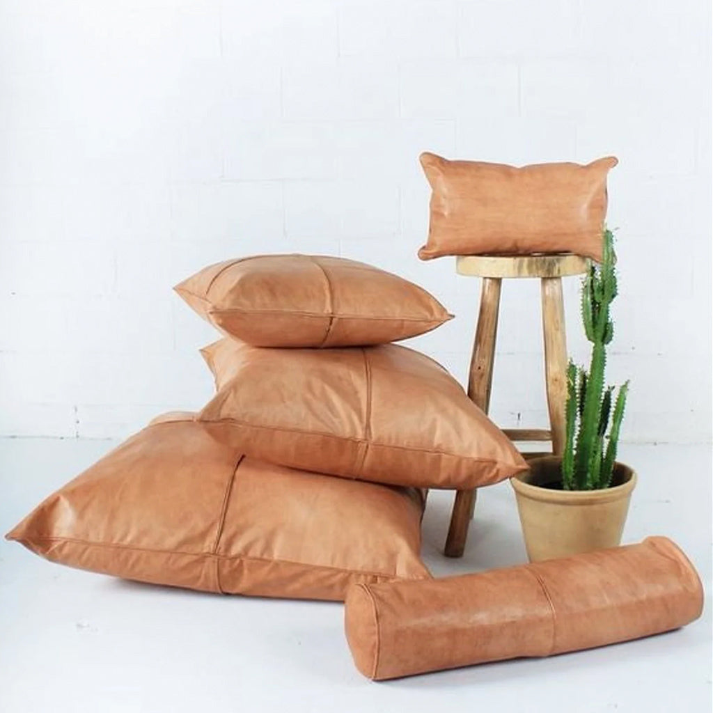 Handcrafted Moroccan leather throw and lumbar pillows displayed with a wooden stool and cactus.