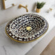 Top view of a handcrafted brass drop-in sink with a black and white mosaic design, installed on a marble countertop in a modern bathroom