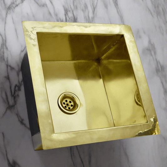 Close-up of a handcrafted brass kitchen sink, highlighting the polished brass material and square design suitable for undermount installation